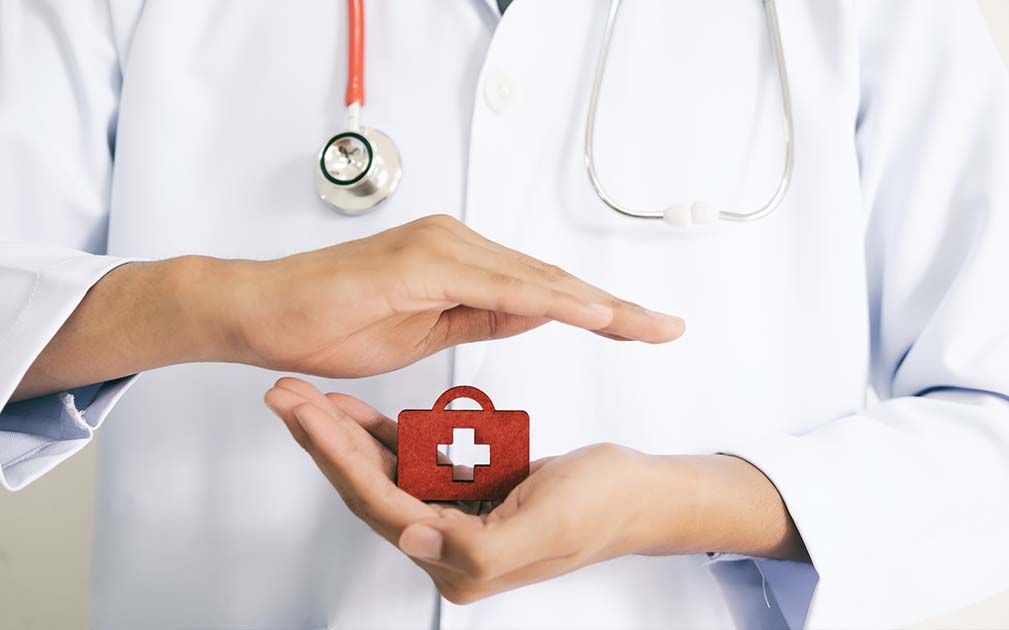 A doctor in a white coat holding a small red first-aid case.